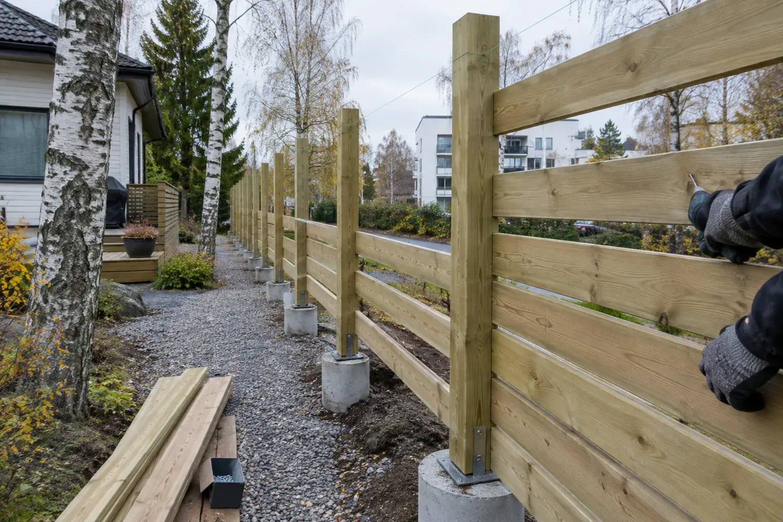 Puuaidan rakentaminen helsinkiläisellä pihalla, tolpat betonissa ja laudoitus kesken